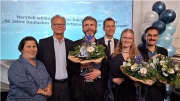 Gruppenfoto bei der Jubiläumsveranstaltung „50 Jahre Deutsches Schifffahrtsmuseum“. Drei ausgezeichnete Personen halten Blumensträuße, umgeben von Gratulanten. Im Hintergrund Ballondekoration und eine Leinwand mit Veranstaltungsaufschrift.