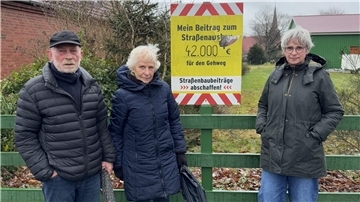 Ehepaar Krüger und Tochter Birte stehen vor ihrem Schild gegen den Straßenbau