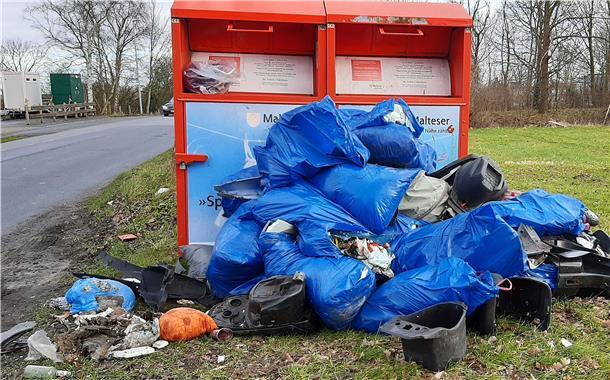 Mehrere Tüten mit Müll liegen vor zwei Altkleidercontainern.