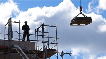 Ein Arbeiter dirigiert auf einer Baustelle einen Kran.