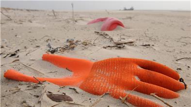 Ein Arbeitshandschuh und ein Plastikkanister liegen an einem Strand im Sand. Solchen Unrat finden auch die freiwilligen Müllsammler der Sauberhaften Küste. 