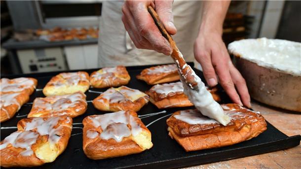 Ein Bäckermeister pinselt Zuckerguss auf süßes Gebäck in seiner Backstube.