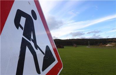 Ein Baustellenschild steht vor einer grünen Wiese: Die Gemeinde Breddorf möchte Bauland anbieten. Doch das Verfahren verzögert sich.
