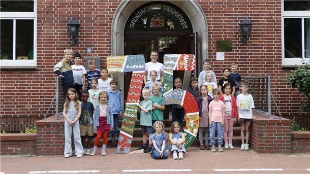 Eine Schulklasse mit einer großen 75 vor einer Schule.