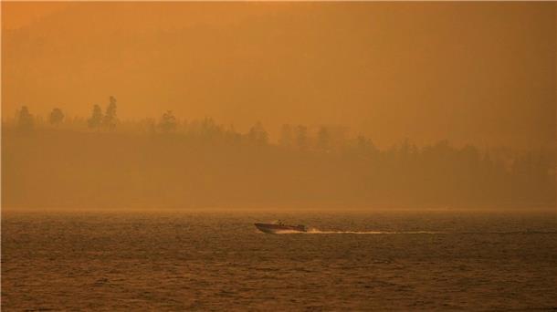 Ein Boot fährt auf dem Okanagan-See, während der Rauch des McDougall-Creek-Wildfeuers über dem Gebiet liegt.
