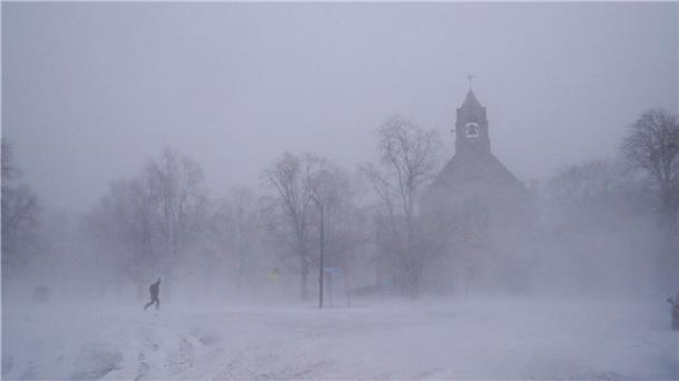 Ein einsamer Fußgänger in Schneeschuhen geht über den Colonial Circle, während sich die St. John’s Grace Episcopal Church in Buffalo  inmitten eines Schneesturms aus dem Schneetreiben erhebt.