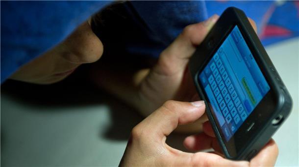 Ein elfjähriger Junge liegt unter der Bettdecke und schreibt auf einem Smartphone eine SMS. Kinder unter 13 Jahren sollten Experten zufolge keinen Zugang zu derartigen Medien haben.