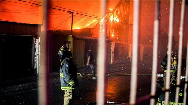 Zahl der Toten bei Waldbränden in Chile steigt auf 112 Ein Feuerwehrmann blickt nach oben, als die Flammen eines Waldbrandes auf Gebäude übergreifen.