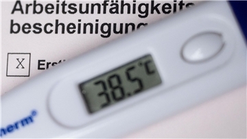 Ein Fieberthermometer liegt auf einer Arbeitsunfähigkeitsbescheinigung.