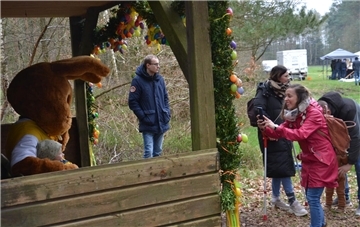 Hanni Hase sitzt mit einem Kind auf einer Bank. Die Mutter fotografiert die beiden.