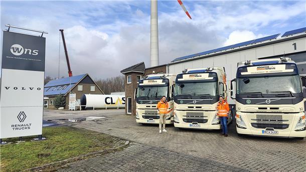 Zwei Männer stehen auf einem Lkw Hof vor drei Elektro-Lkws
