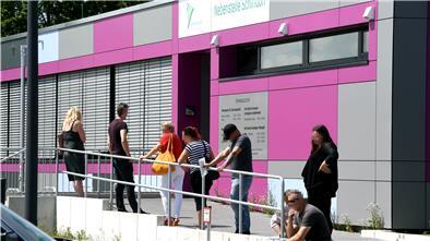 Menschen warten in einer Schlange vor einem Gebäude.
