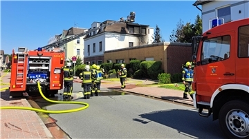 Bild von einem brennenden Haus, zwei Feuerwehrfahrzeugen und Feuerwehrleuten in der Langen Straße in Blexen
