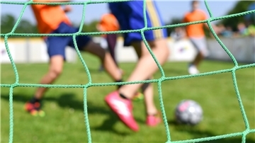  Kinder spielen auf einem Sportplatz Fußball. 