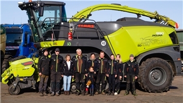 Eine größere Menschengruppe steht vor einer großen landwirtschaftlichen Maschine.