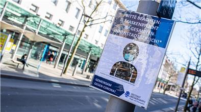 Ein Informationsschild in der Fußgängerzone weist auf die Maskenpflicht in der Innenstadt hin. Aber nicht alle Menschen halten sich daran.