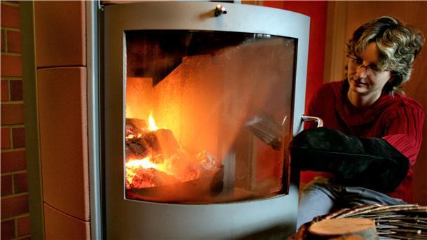 Eine Frau befüllt einen Kaminofen mit Holz.