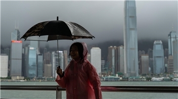 Ein Mädchen hält einen Regenschirm in Tsim Sha Tusi vor dem Victoria Harbor und der Skyline von Hongkong während des Taifuns „Tapah“.