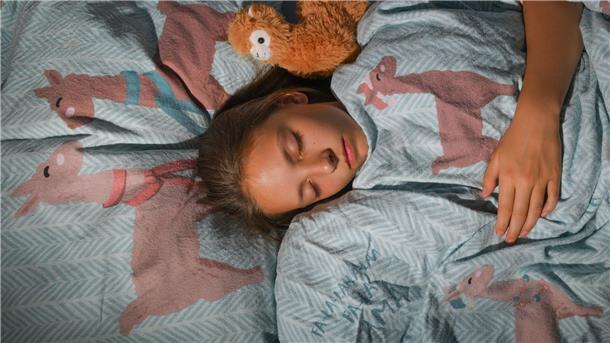 Ein Mädchen liegt eingekuschelt im Bett. Sich morgens aufzuraffen, fällt meist schwer. Fachleute aber raten vom Schlummern ab.
