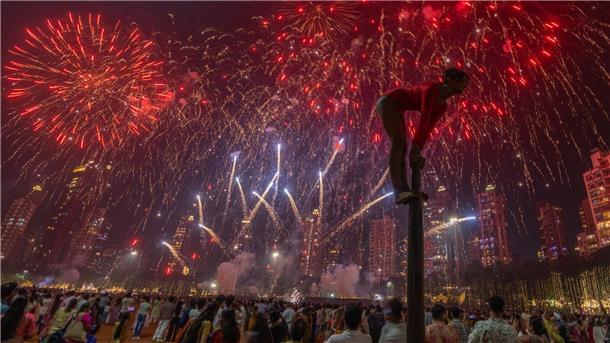 Ein Mädchen performt auf einer Mallakhamb-Stange, während Feuerwerkskörper den Himmel während des Diwali-Lichterfestes in Mumbai erhellen.