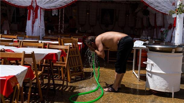 Ein Mann erfrischt sein Gesicht mit einem Wasserschlauch.