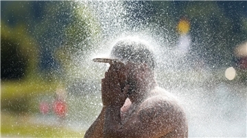Ein Mann erfrischt sich an einem Badesee unter einer kalten Dusche.