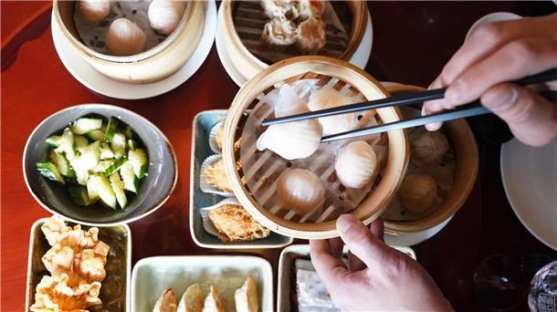 Ein Mann greift mit Essstäbchen nach Dim sum, gedämpften Teigtaschen, in einem Bambuskorb.