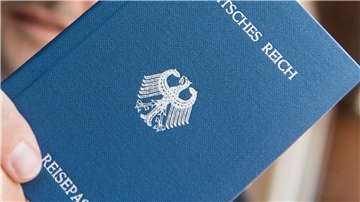 Ein Mann hält ein Heft mit dem Aufdruck „Deutsches Reich Reisepass“ in der Hand.