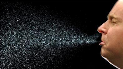 Ein Mann niest. Beim Niesen fliegen viele Tröpfchen durch die Luft. Auf diese Weise kann sich auch das neuartige Coronavirus Sars-CoV-2 verbreiten.