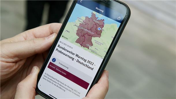 Ein Mitarbeiter des Bundeskanzleramts hält sein Mobiltelefon in der Hand.