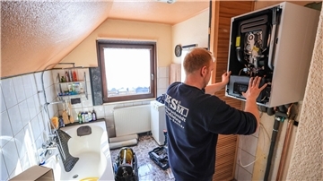 Ein Mitarbeiter einer Sanitär- und Heizungsbaufirma installiert eine moderne Gasbrennwerttherme in einem Einfamilienhaus.