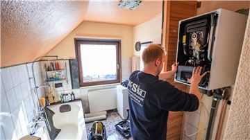 Ein Mitarbeiter einer Sanitär- und Heizungsbaufirma installiert eine moderne Gasbrennwerttherme in einem Einfamilienhaus.