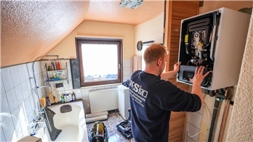 Ein Mitarbeiter einer Sanitär- und Heizungsbaufirma installiert eine moderne Gasbrennwerttherme in einem Einfamilienhaus.