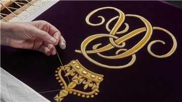 Ein Mitglied der Royal School of Needlework stickt den Schriftzug von Queen Camilla von Hand auf deren Robe.