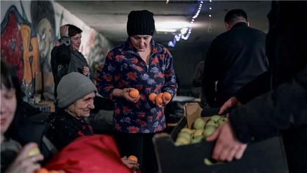 Ein Polizist in Awdijiwka beschenkt Menschen mit Mandarinen und Äpfeln in der Vorweihnachtszeit in einem als Bunker genutzten Keller eines Wohnhauses.