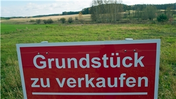 Ein Schild mit der Aufschrift „Grundstück zu verkaufen" steht an einer Straße.