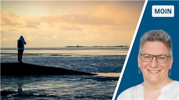 Ein Spaziergänger steht im Watt vor Cuxhaven und fotografiert die Insel Neuwerk.