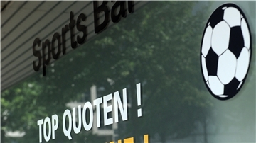 Ein Sportwettenladen wirbt mit aufgeklebten Slogans an einer Fensterscheibe.