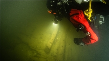 Ein Taucher benutzt in der Trave bei der Begutachtung von Planken eines Schiffswracks eine Unterwasserlampe. Taucher haben auf dem Grund der Trave ein rund 400 Jahre altes Wrack eines Hanseschiffes aus dem 17. Jahrhundert entdeckt.