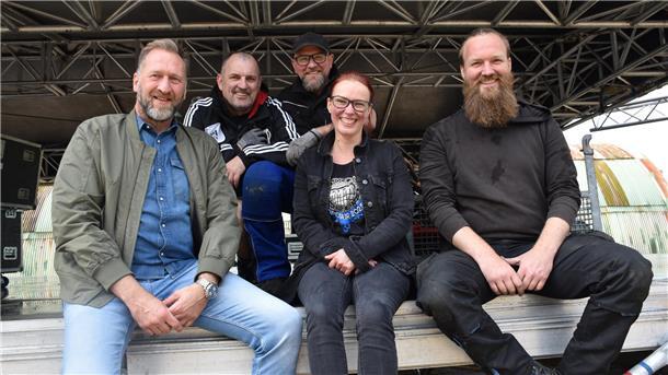 Menschen sitzen auf einer Bühne bei deren Aufbau