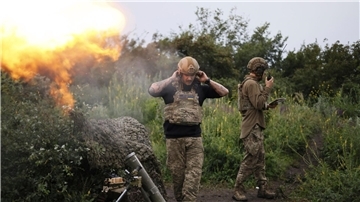 Ein ukrainischer Soldat während eines Funkgesprächs, während ein anderer Soldat 82-mm-Mörser auf russische Stellungen feuert.