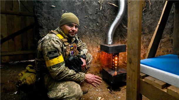 Ein ukrainischer Soldat wärmt sich an einem Ofen.