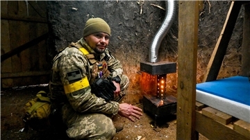 Ein ukrainischer Soldat wärmt sich an einem Ofen.