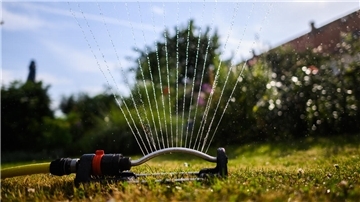 Ein Wassersprenger bewässert den Garten eines Reihenhauses.
