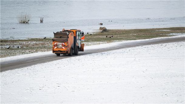 Ein Winterdienst-Fahrzeug fährt auf dem Radweg an den verschneiten Elbwiesen in Dresden entlang.