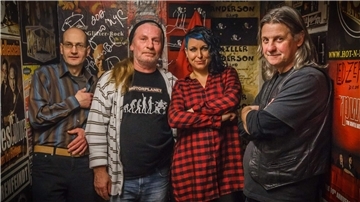 Bandfoto von Motorplanet: Drei Männer und eine Frau stehen in einem Raum mit vielen Bandplakaten.