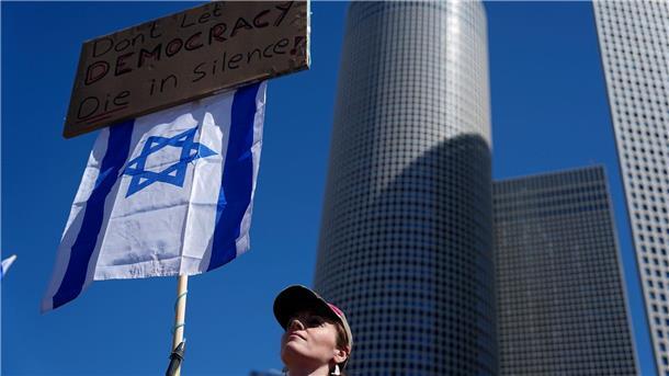 Großer Protesttag gegen Justizreform in Israel Eine Demonstrierende hält eine israelische Flagge und ein Plakat mit der Aufschrift „Lasst die Demokratie nicht schweigend sterben!“.