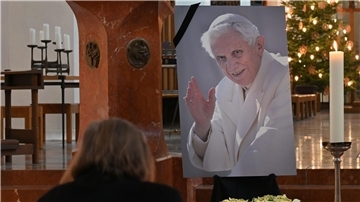 Eine Frau betet in der Frauenkirche in München vor einem Bild des verstorbenen emeritierten Papst Benedikt XVI.