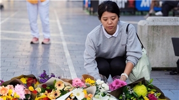 Eine Frau bringt Blumen zu einer improvisierten Gedenkstätte an der Bondi Junction.