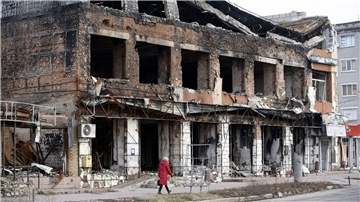 Eine Frau geht an einem durch russischen Beschuss zerstörten Gebäude in der Region Charkiw vorbei.